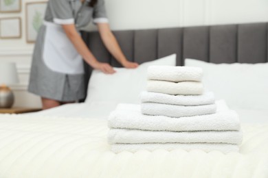 Photo of Chambermaid working in hotel room, focus on stack of terry towels on bed