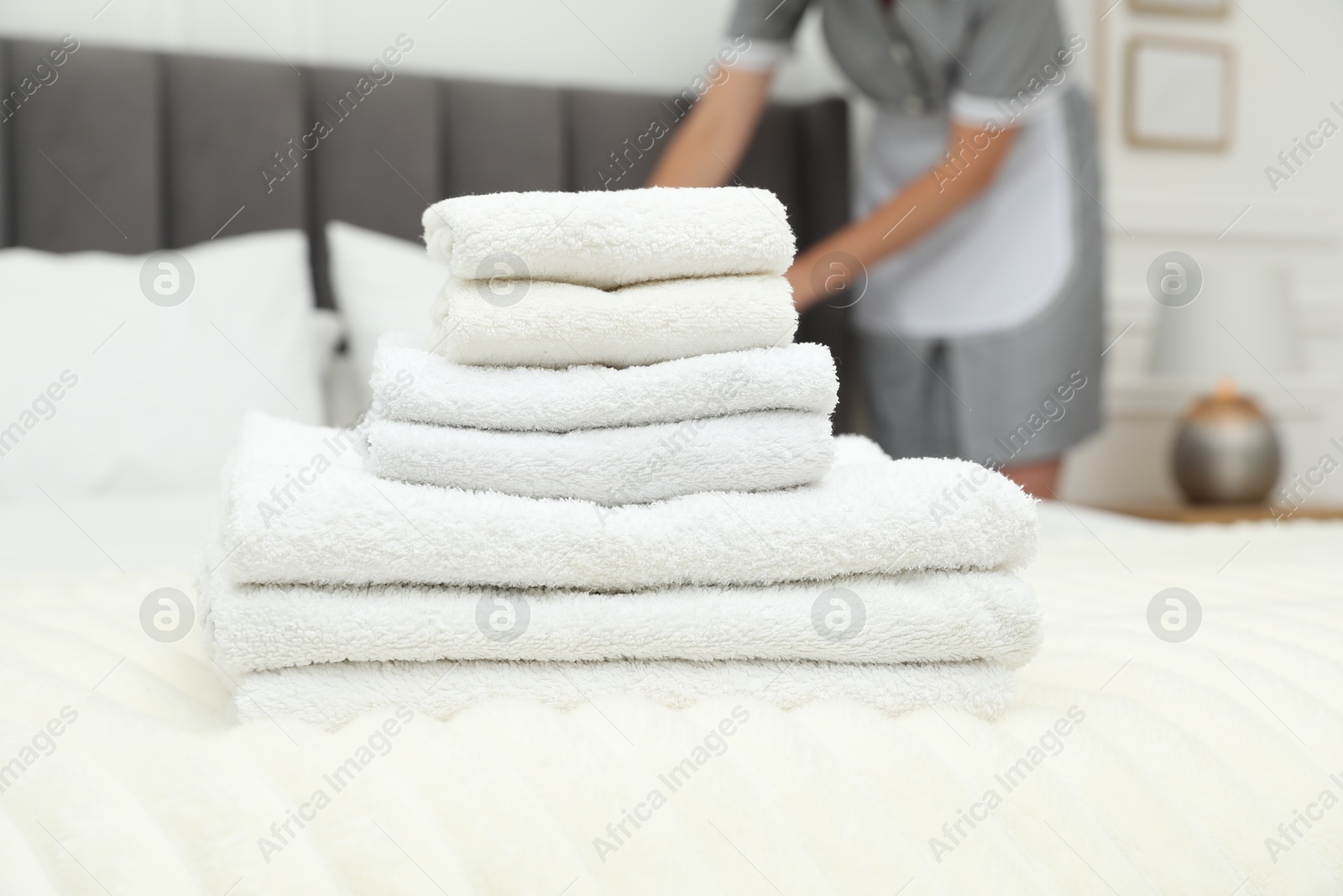 Photo of Chambermaid working in hotel room, focus on stack of terry towels on bed