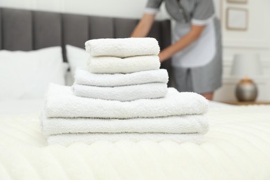 Photo of Chambermaid working in hotel room, focus on stack of terry towels on bed