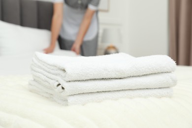 Photo of Chambermaid working in hotel room, focus on stack of terry towels on bed