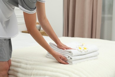 Photo of Chambermaid putting stack of white terry towels and plumeria flowers onto bed indoors, closeup
