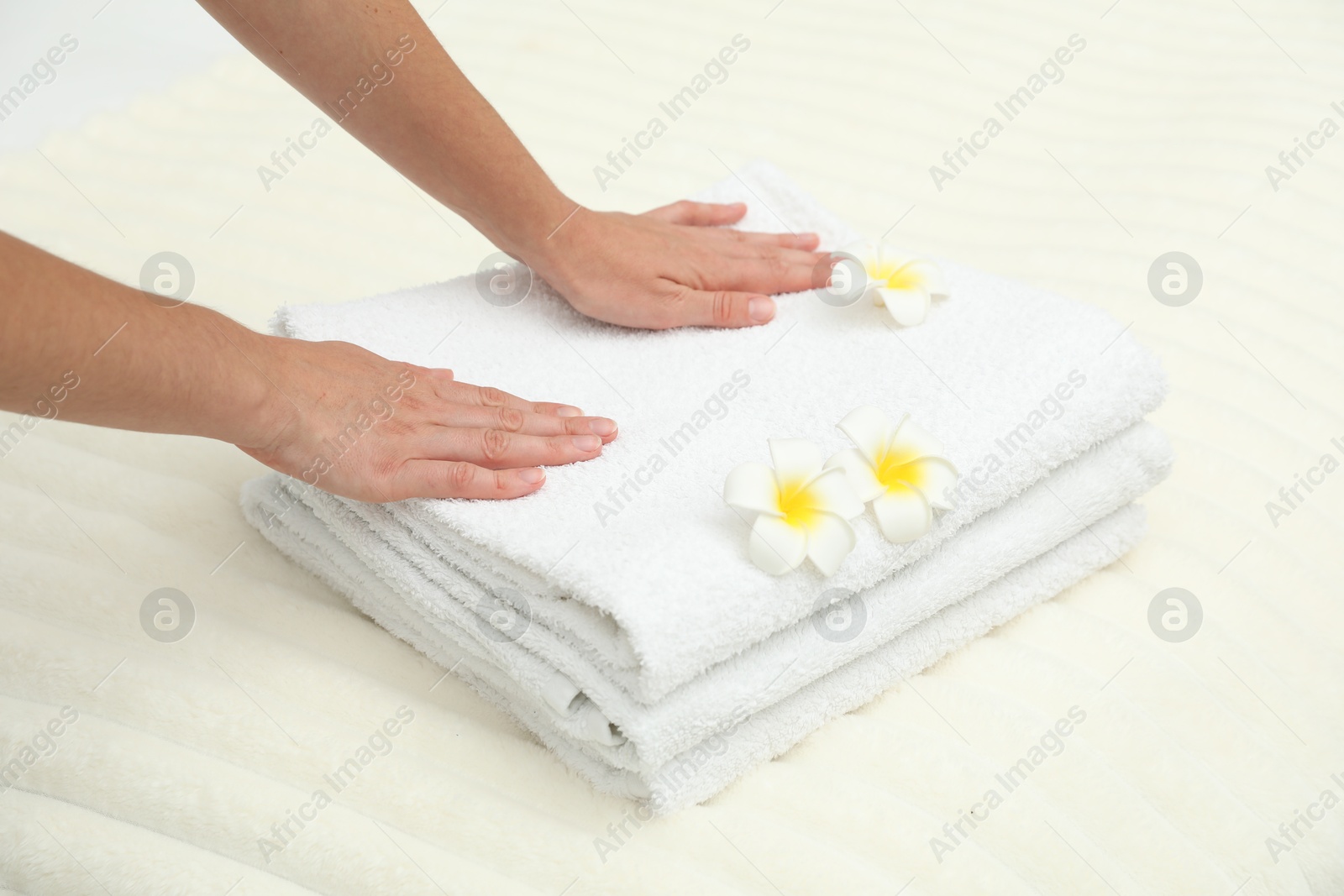Photo of Woman putting stack of white terry towels and plumeria flowers onto bed, closeup