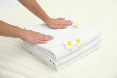 Photo of Woman putting stack of white terry towels and plumeria flowers onto bed, closeup