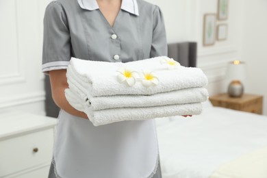 Photo of Chambermaid with stack of white terry towels and plumeria flowers in hotel room, closeup