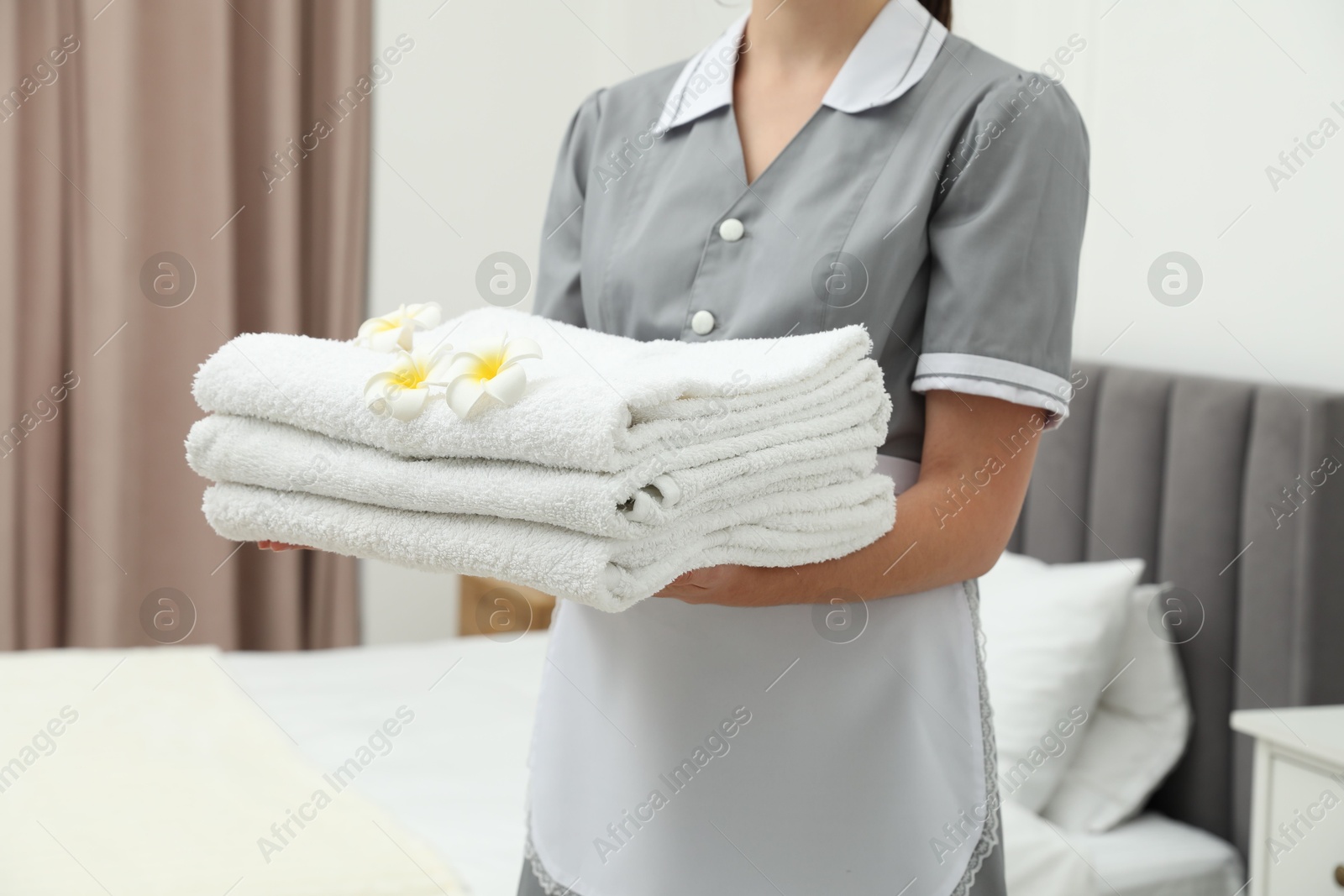Photo of Chambermaid with stack of white terry towels and plumeria flowers in hotel room, closeup