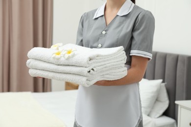 Photo of Chambermaid with stack of white terry towels and plumeria flowers in hotel room, closeup
