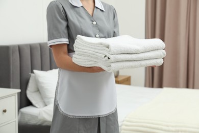 Photo of Chambermaid with stack of white terry towels in hotel room, closeup