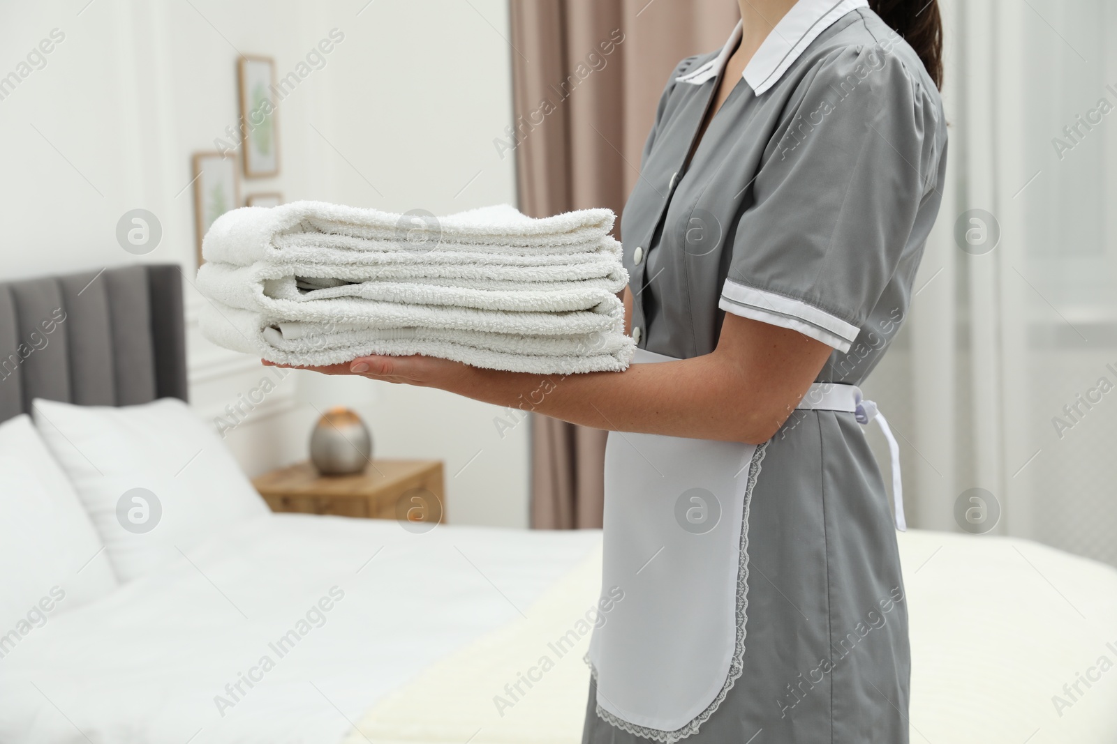 Photo of Chambermaid with stack of white terry towels in hotel room, closeup