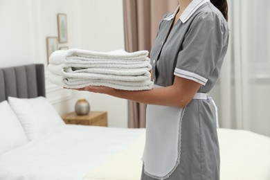 Photo of Chambermaid with stack of white terry towels in hotel room, closeup