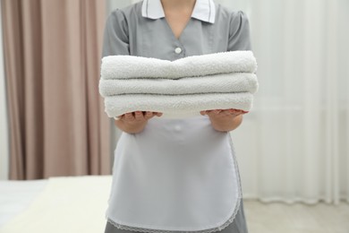 Photo of Chambermaid with stack of white terry towels in hotel room, closeup
