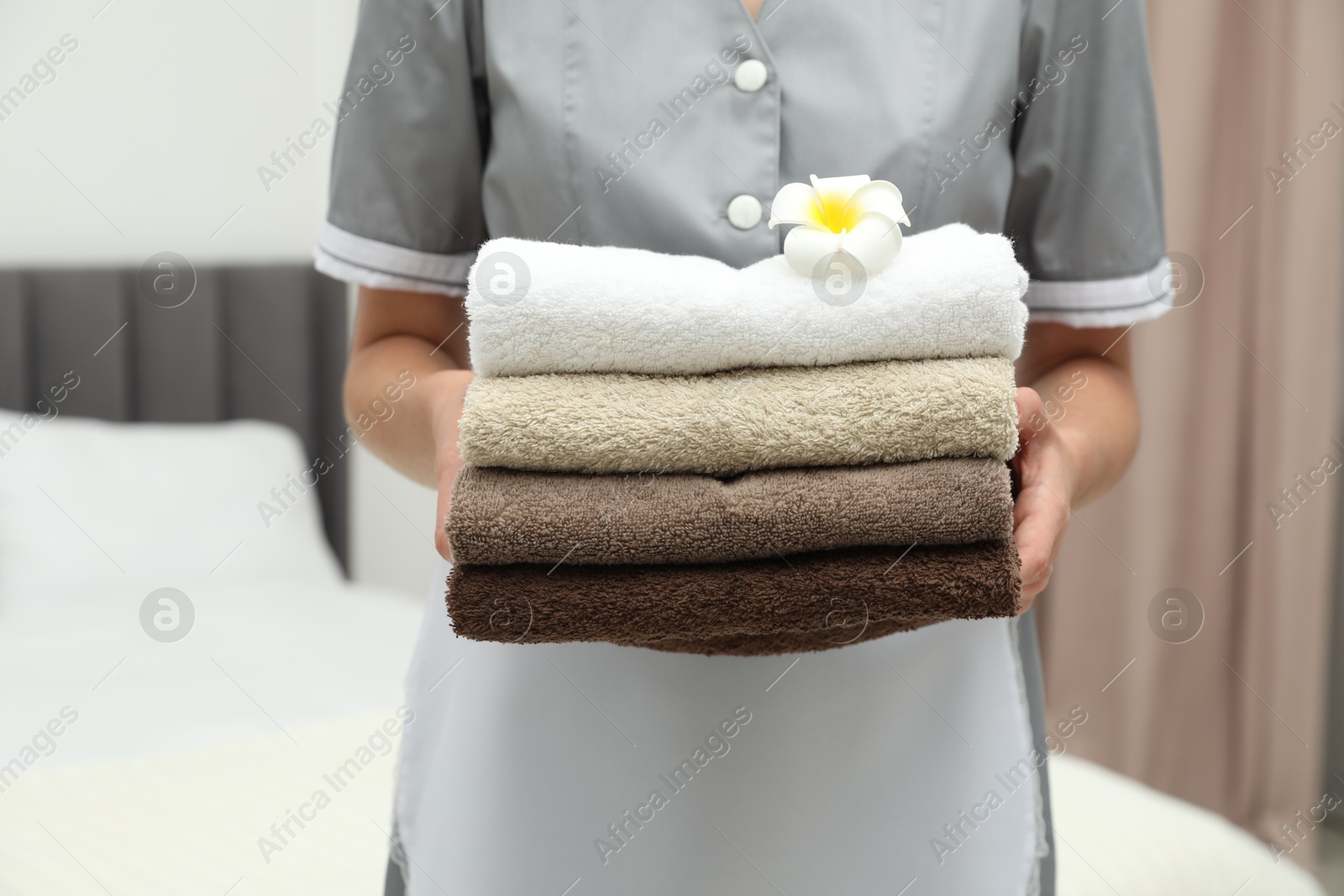 Photo of Chambermaid with stack of terry towels and plumeria flower in hotel room, closeup