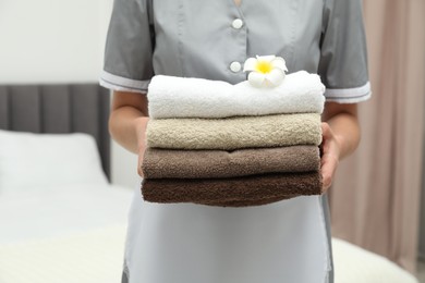 Photo of Chambermaid with stack of terry towels and plumeria flower in hotel room, closeup