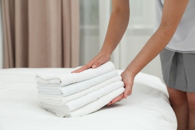 Photo of Chambermaid putting stack of white terry towels onto bed indoors, closeup