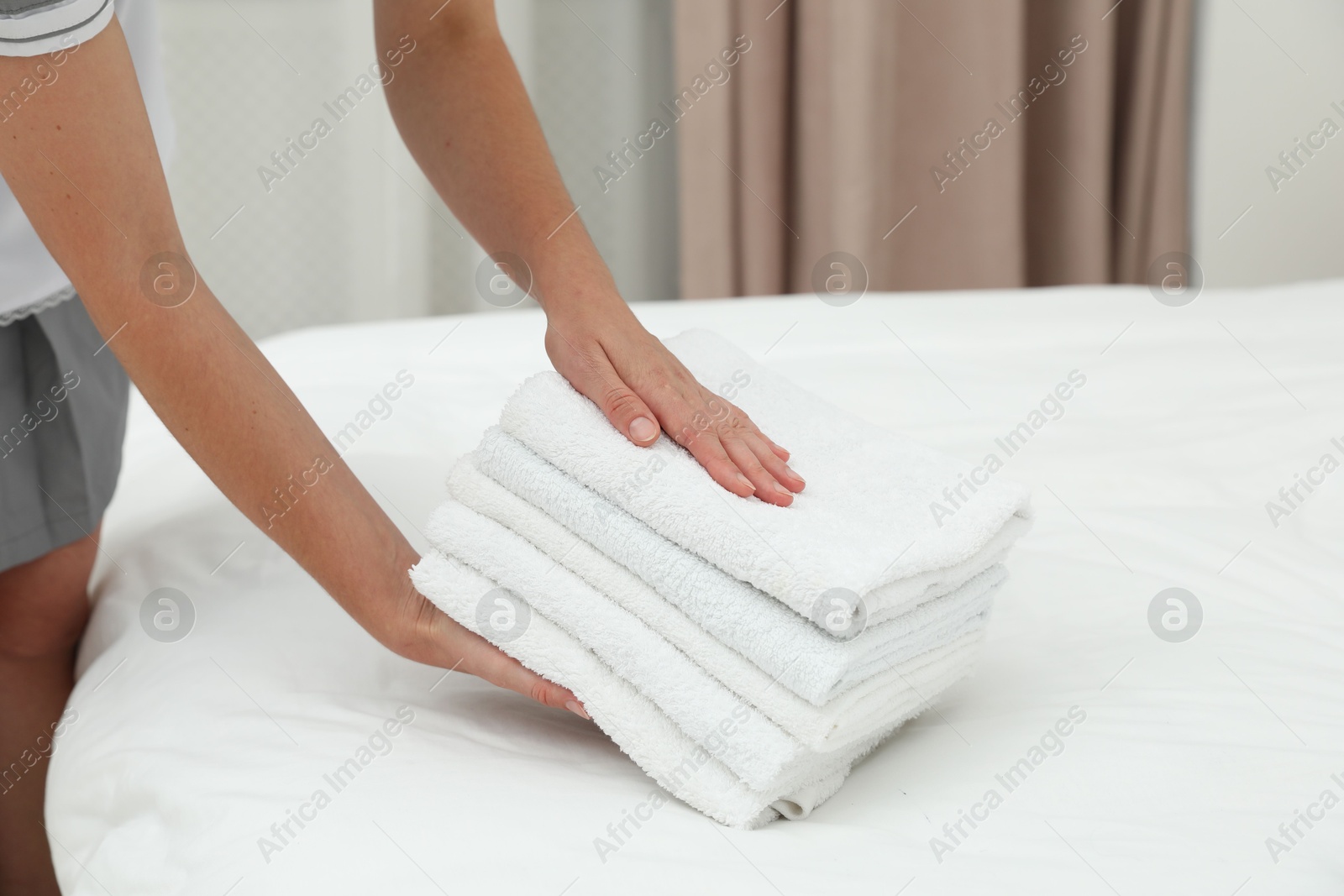 Photo of Chambermaid putting stack of white terry towels onto bed indoors, closeup