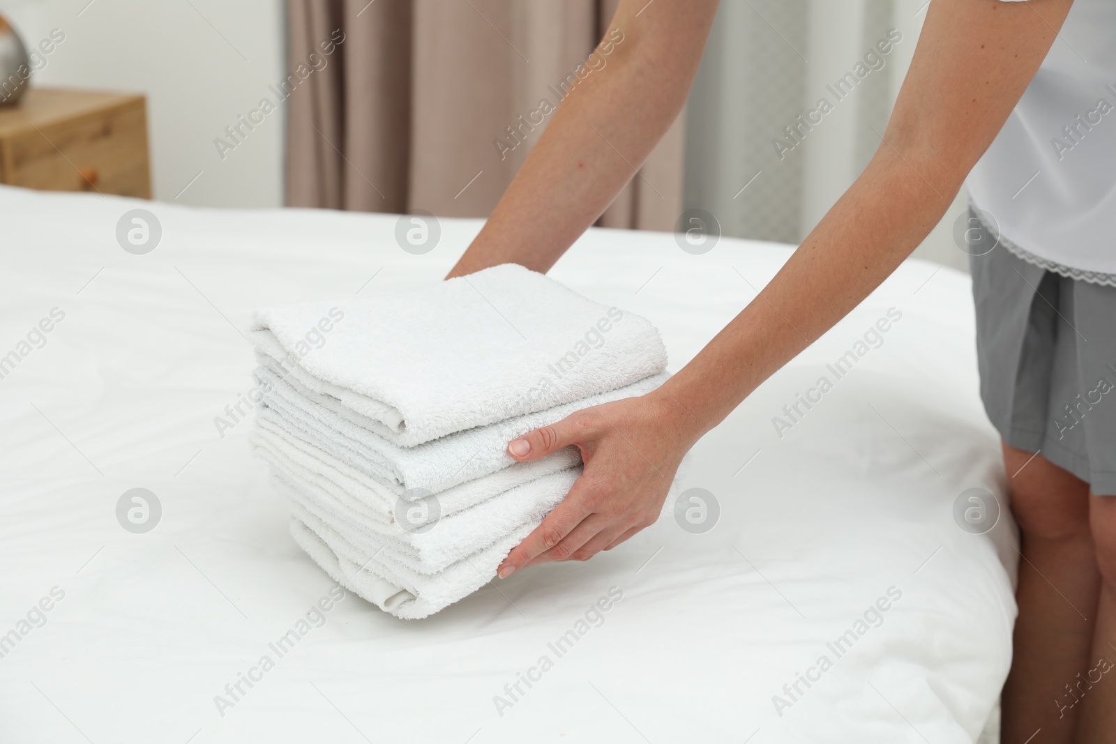 Photo of Chambermaid putting stack of white terry towels onto bed indoors, closeup