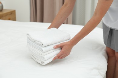 Photo of Chambermaid putting stack of white terry towels onto bed indoors, closeup