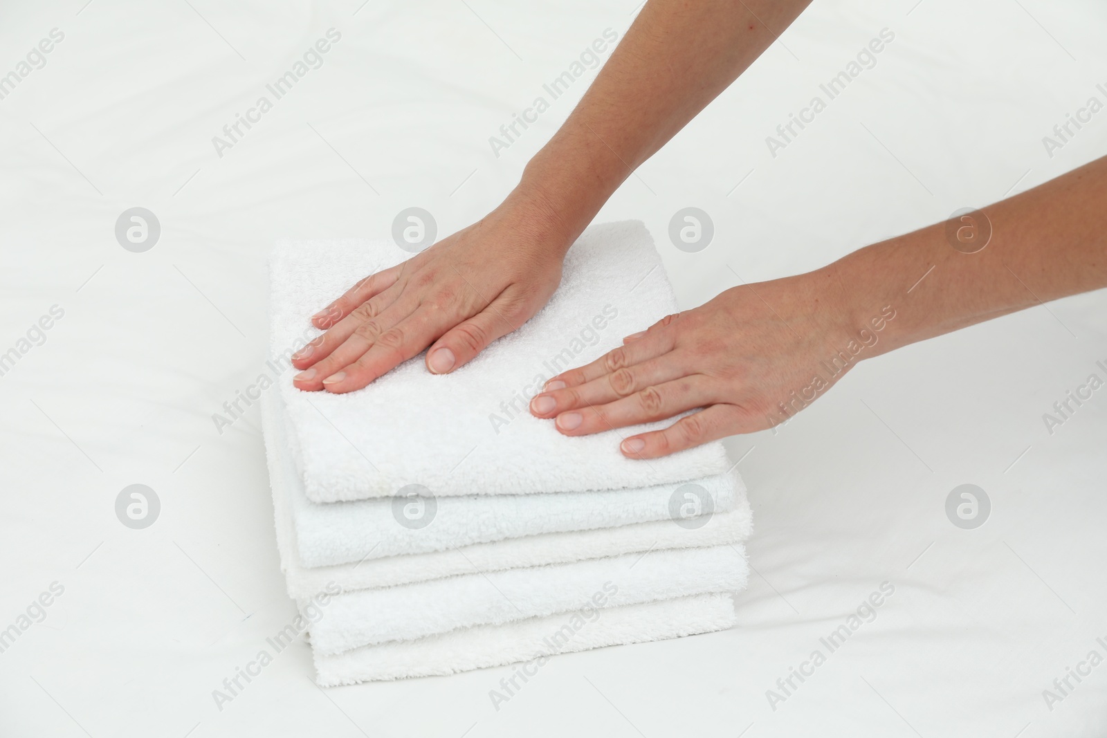 Photo of Woman putting stack of white terry towels onto bed linens, closeup