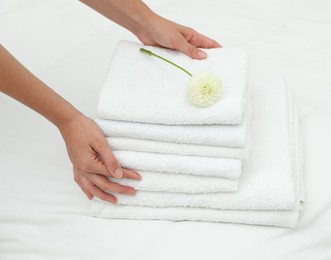 Photo of Woman putting stack of white terry towels and dahlia flower onto bed linens, closeup