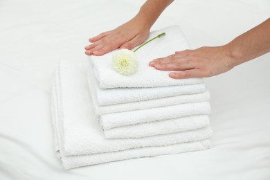 Photo of Woman putting stack of white terry towels and dahlia flower onto bed linens, closeup