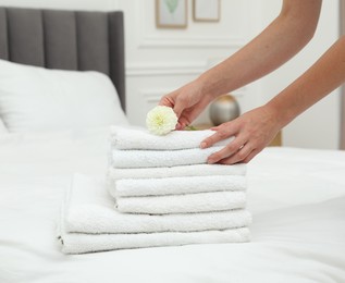 Photo of Woman putting dahlia flower onto stack of white terry towels on bed indoors, closeup