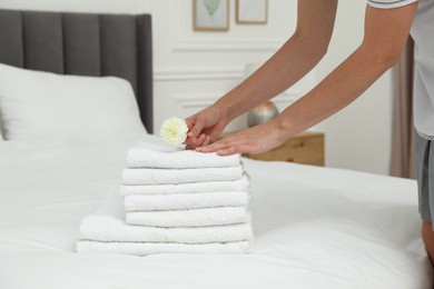 Photo of Chambermaid putting dahlia flower onto stack of white terry towels on bed in hotel room, closeup