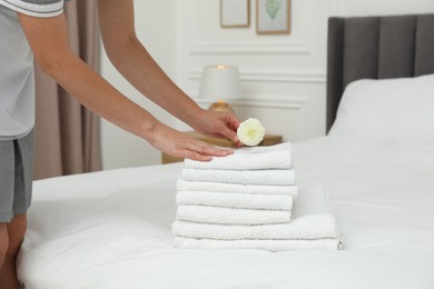 Photo of Chambermaid putting dahlia flower onto stack of white terry towels on bed in hotel room, closeup