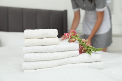 Photo of Chambermaid working in hotel room, focus on stack of terry towels and beautiful flowers on bed