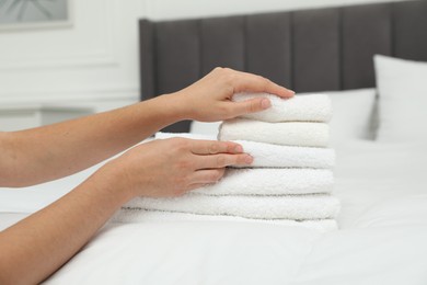 Photo of Woman putting stack of white terry towels onto bed indoors, closeup