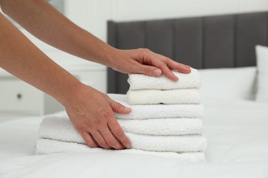 Photo of Woman putting stack of white terry towels onto bed indoors, closeup