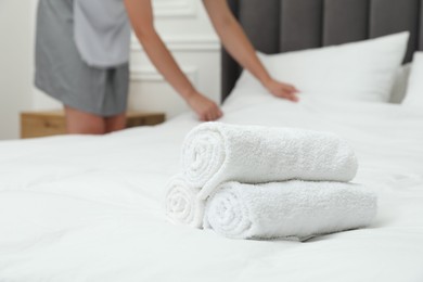 Photo of Chambermaid working in hotel room, focus on stack of terry towels on bed