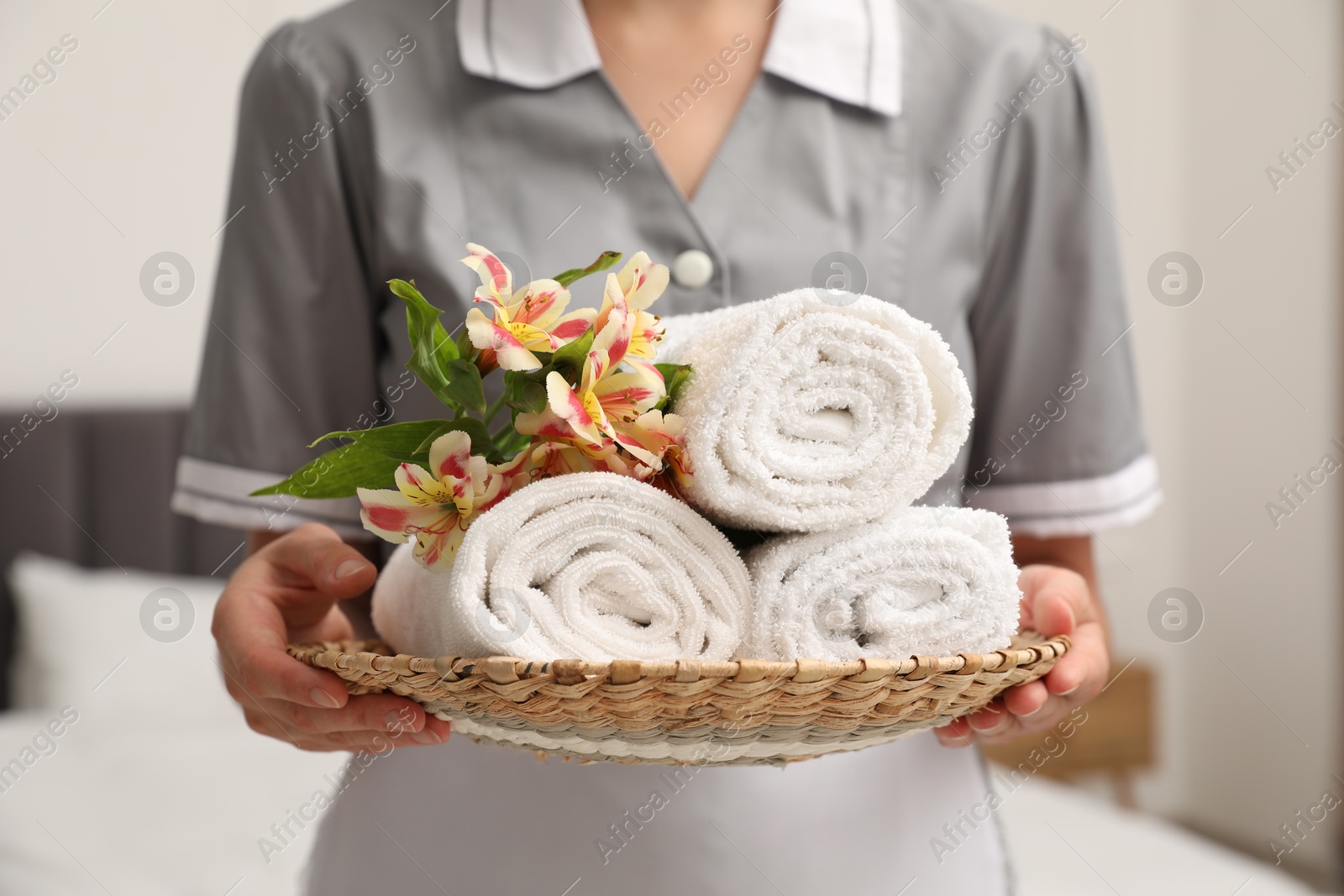 Photo of Chambermaid with stack of terry towels and beautiful flowers in hotel room, closeup