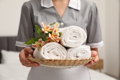 Photo of Chambermaid with stack of terry towels and beautiful flowers in hotel room, closeup