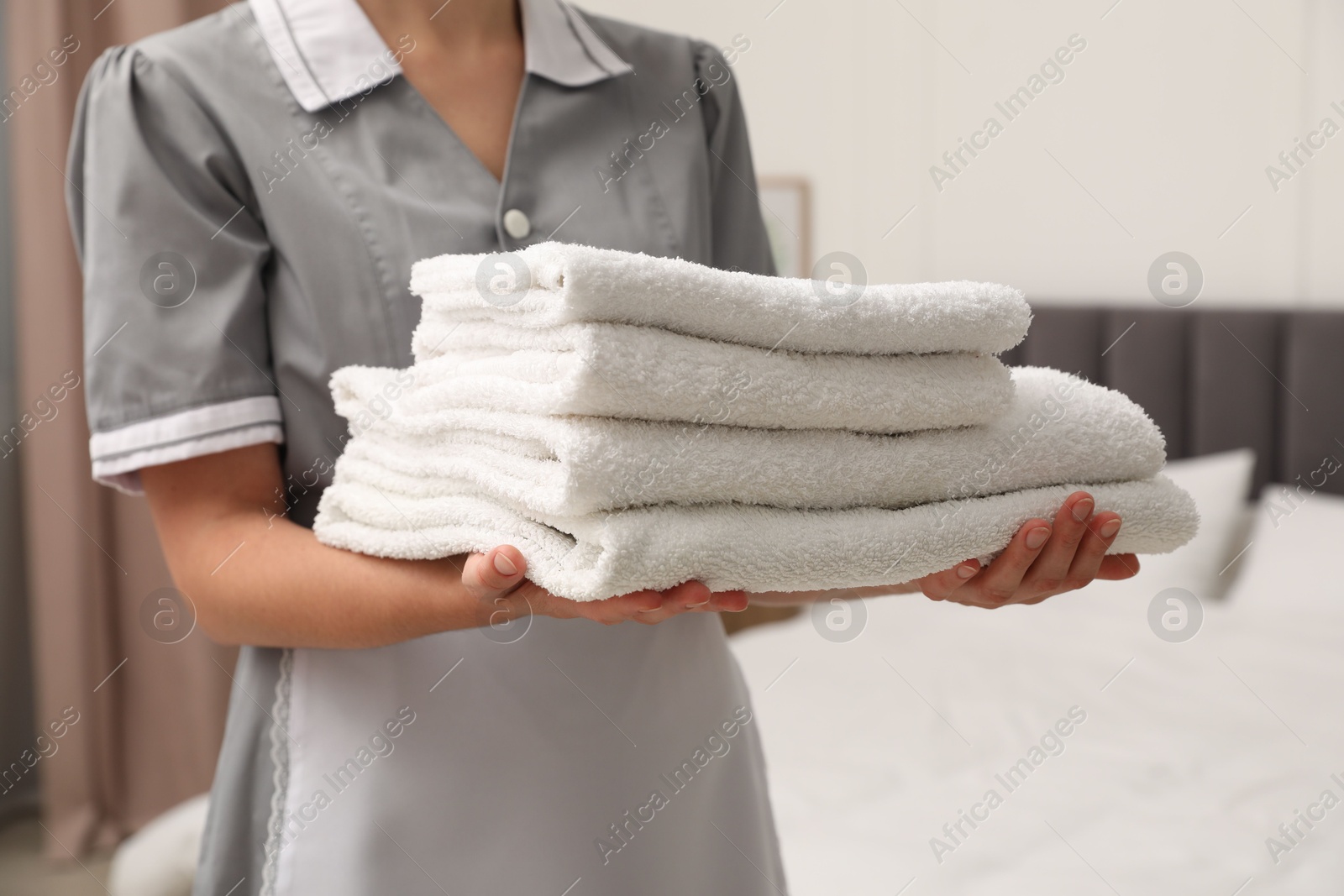 Photo of Chambermaid with stack of white terry towels in hotel room, closeup
