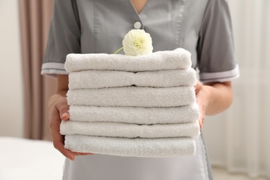 Photo of Chambermaid with stack of white terry towels and dahlia flower in hotel room, closeup