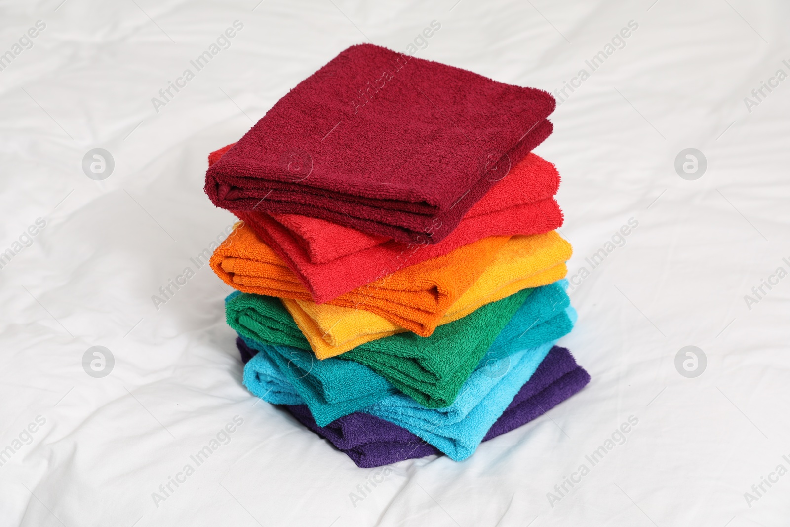 Photo of Stack of bright terry towels on bed linens, closeup