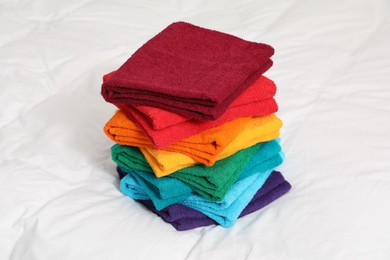 Photo of Stack of bright terry towels on bed linens, closeup