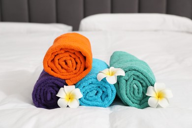Photo of Bright terry towels and plumeria flowers on bed, closeup