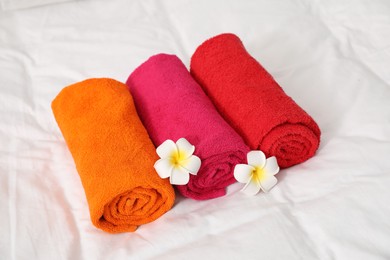 Photo of Bright terry towels and plumeria flowers on bed linens, closeup