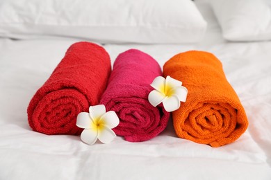Photo of Bright terry towels and plumeria flowers on bed linens, closeup