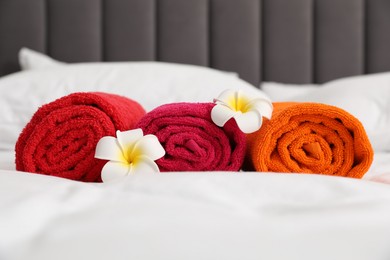 Photo of Bright terry towels and plumeria flowers on bed, closeup