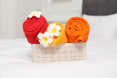 Photo of Bright terry towels and plumeria flowers in storage box on bed indoors, closeup