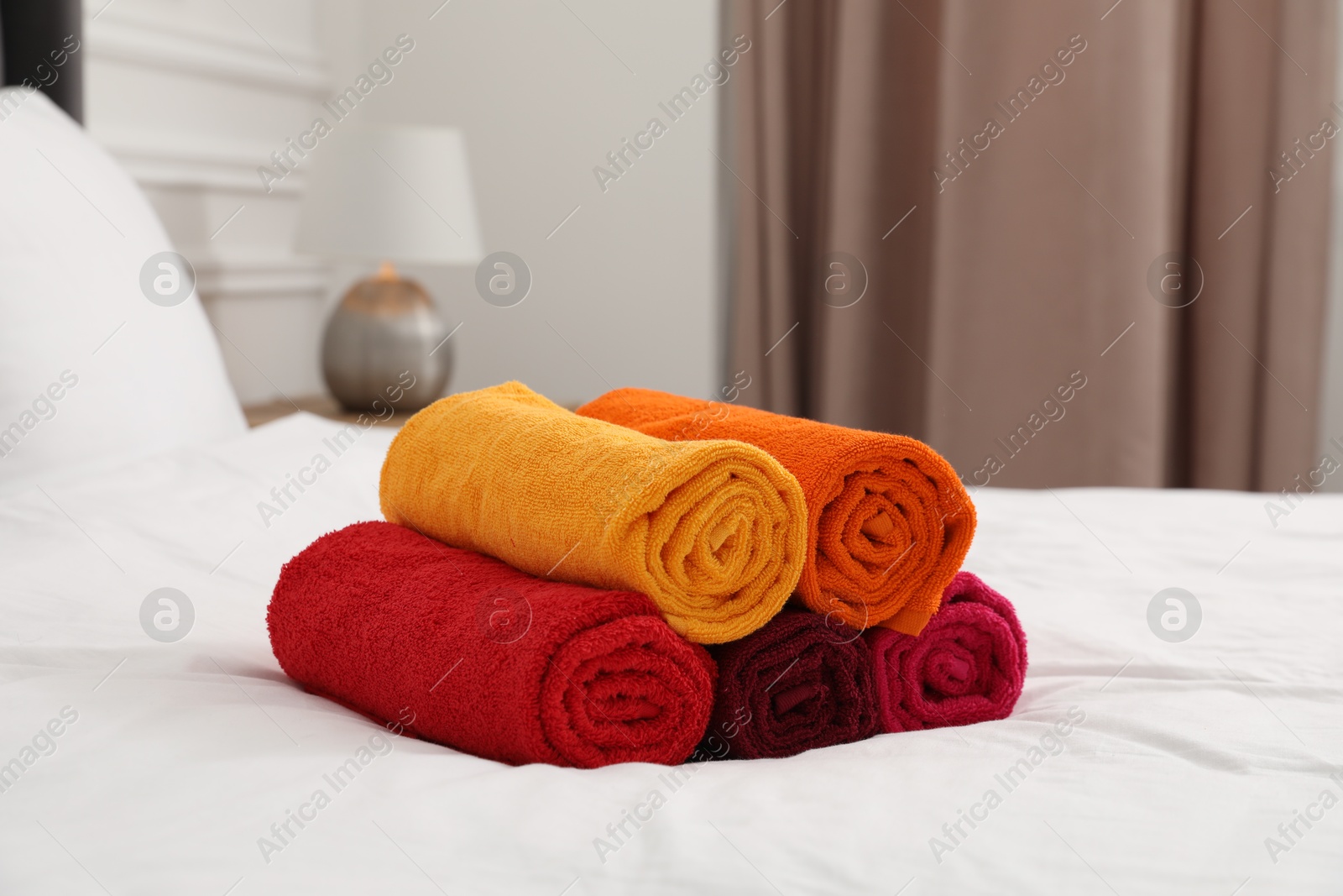 Photo of Rolled bright terry towels on bed indoors, closeup
