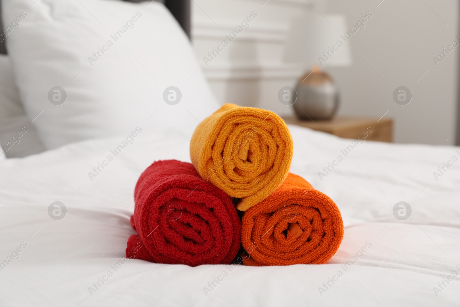 Photo of Rolled bright terry towels on bed indoors, closeup