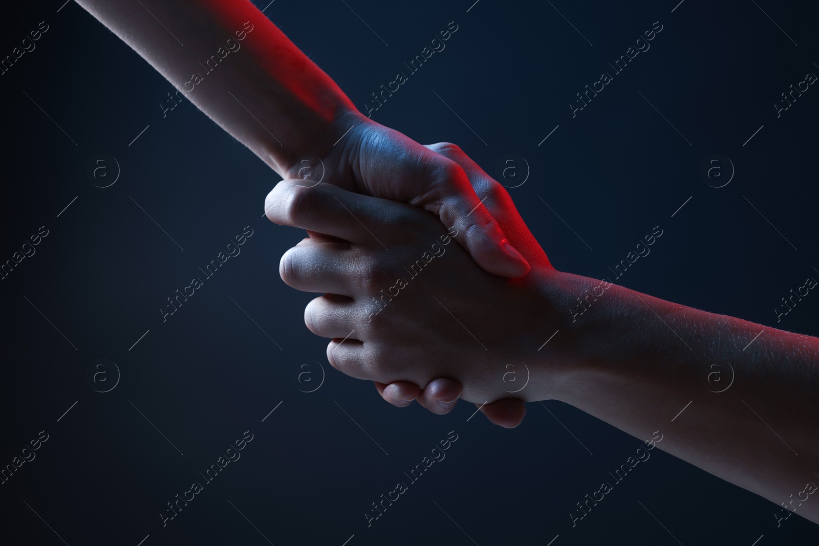 Photo of People holding hands on dark blue background, closeup