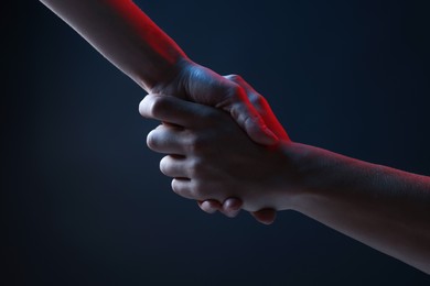 Photo of People holding hands on dark blue background, closeup