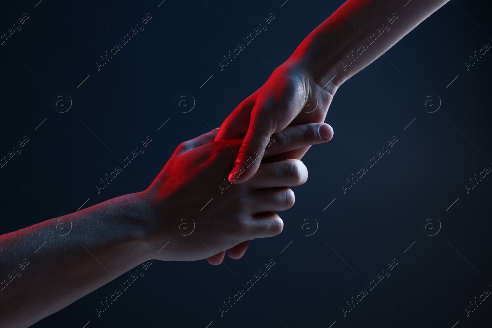 Photo of People holding hands on dark blue background, closeup