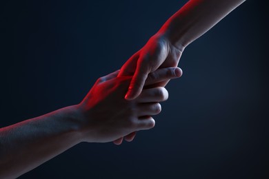 Photo of People holding hands on dark blue background, closeup