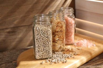 Photo of Different aromatic spices in glass jars on wooden table, closeup