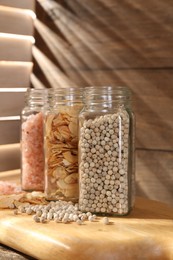 Photo of Different aromatic spices in glass jars on wooden table, closeup