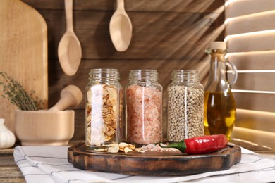 Photo of Different aromatic spices in glass jars on wooden table, closeup